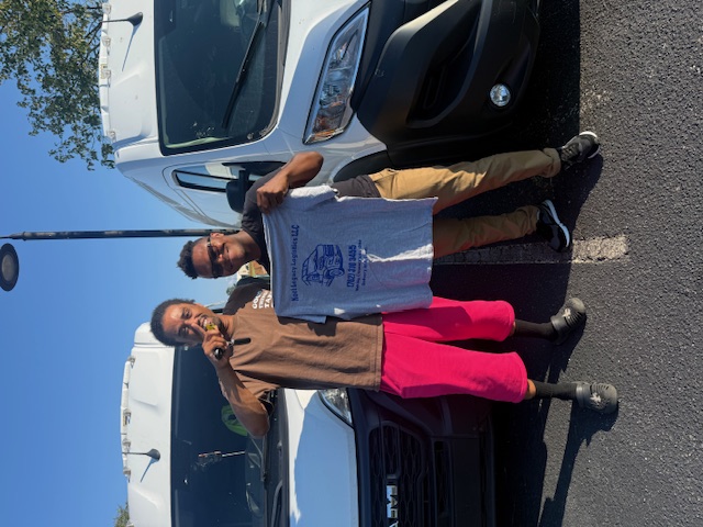 Two people standing between Noel cargo vans, holding a company shirt